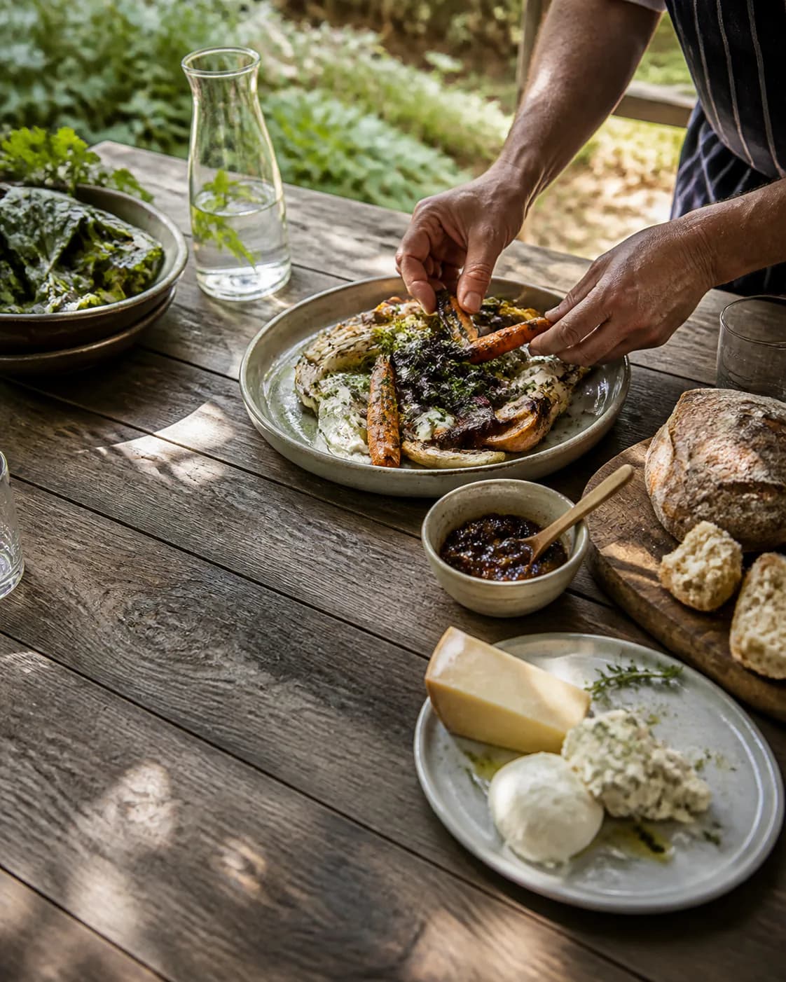 A cook serving a rustic table of seasonal food and fresh bread